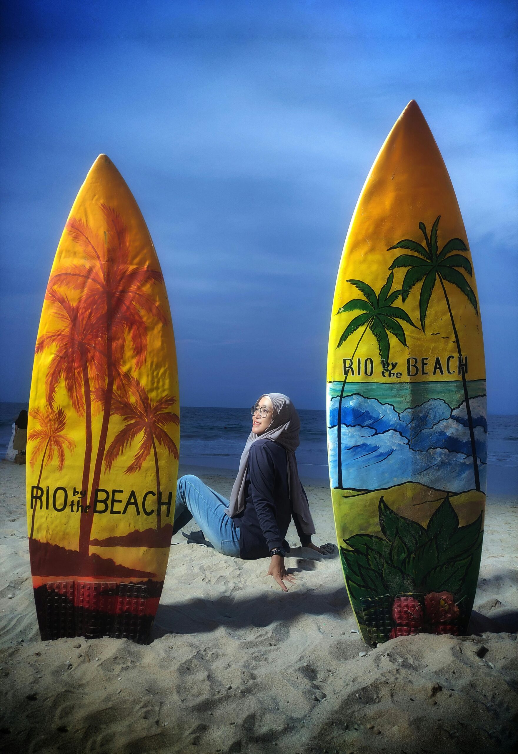 A woman relaxes on a beach with colorful surfboards and a clear sky.