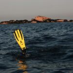 A diver in ocean waters with prominent yellow flippers, exploring near rocky islands.