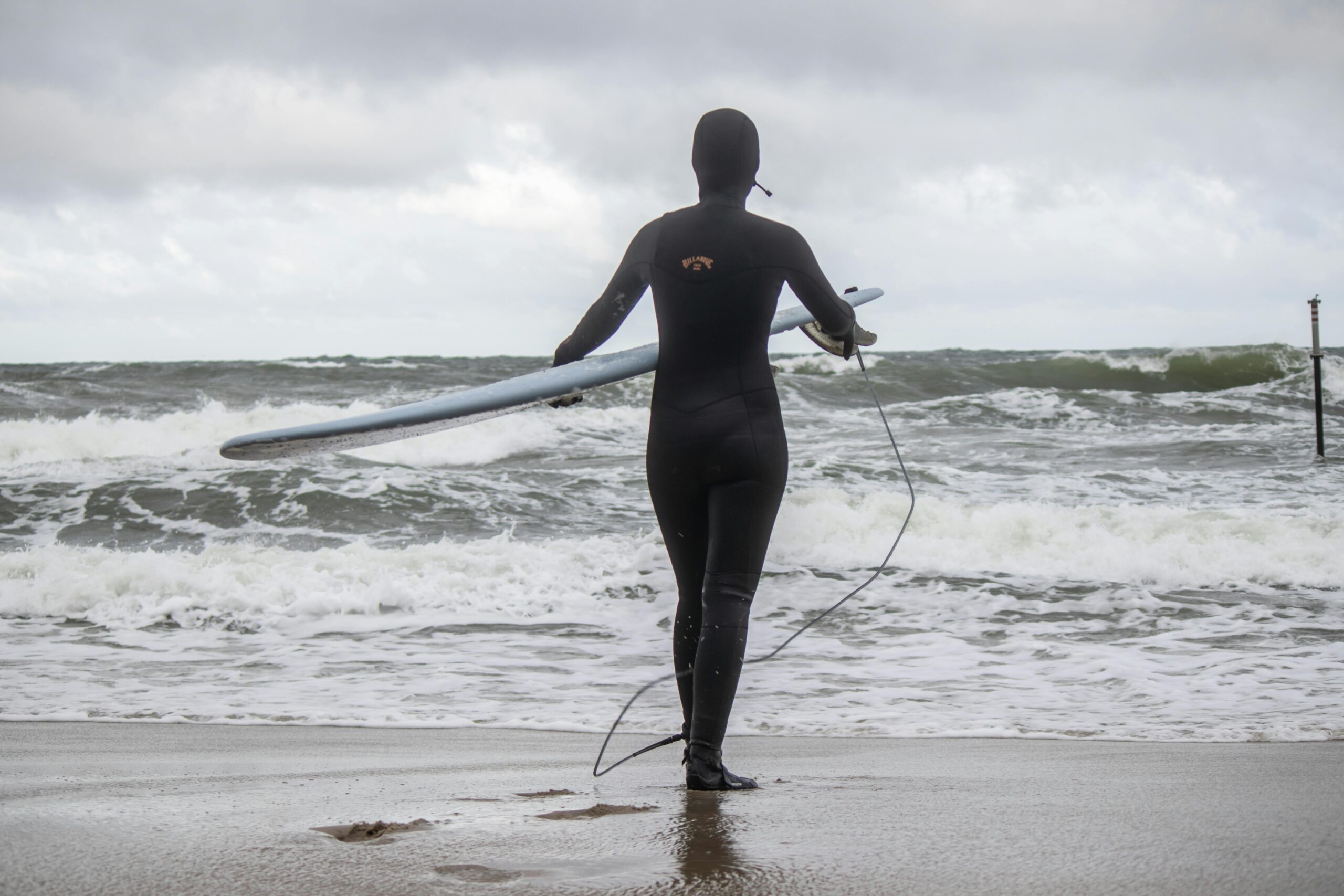 A determined surfer holding a surfboard, facing the rough sea at Jastrzębia Góra, Poland.