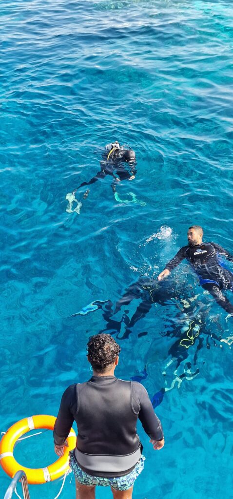 Scuba divers swim in vibrant blue ocean waters, guided by an instructor from a boat.