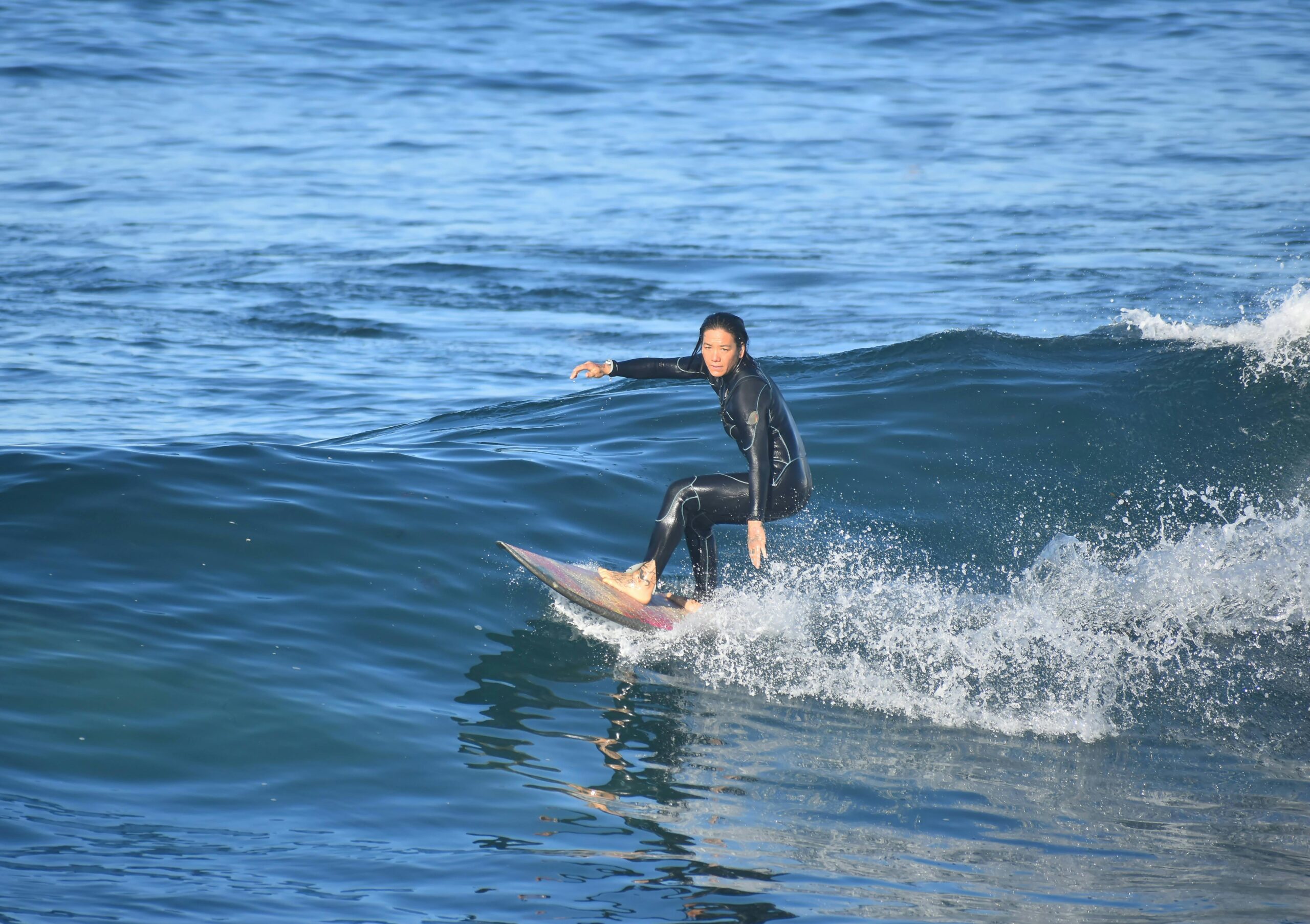 A female surfer skillfully rides a wave in a calm ocean setting, showcasing balance and control.